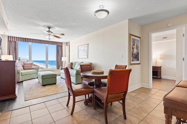 tiled dining area with a water view, ceiling fan, and a textured ceiling