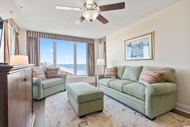 living room with a textured ceiling, light wood-type flooring, ceiling fan, and a water view