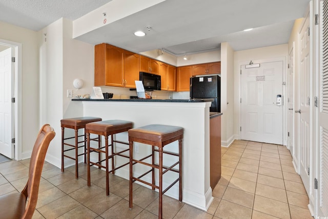 kitchen featuring light tile patterned floors, black appliances, kitchen peninsula, and a kitchen bar