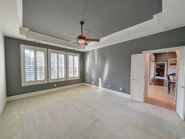 spare room with ceiling fan, light colored carpet, a tray ceiling, and crown molding