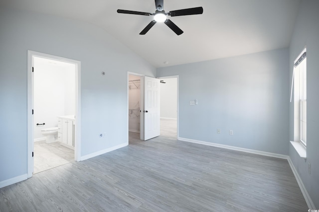 unfurnished bedroom featuring baseboards, a spacious closet, vaulted ceiling, light wood-type flooring, and a closet