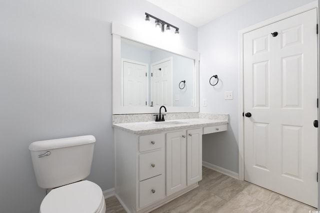 half bath with baseboards, vanity, and toilet