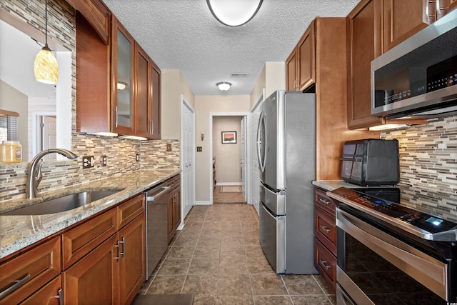 kitchen with sink, light stone counters, hanging light fixtures, appliances with stainless steel finishes, and backsplash