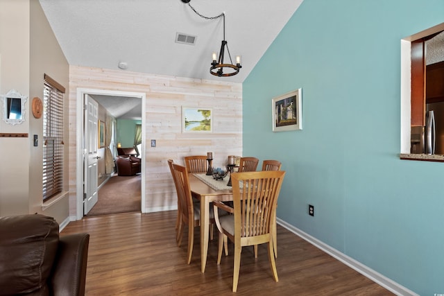 dining space featuring vaulted ceiling, dark hardwood / wood-style floors, wooden walls, a notable chandelier, and a textured ceiling