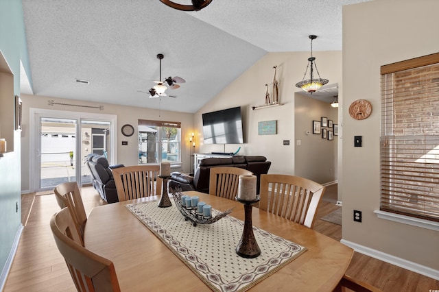 dining space with ceiling fan, vaulted ceiling, light hardwood / wood-style floors, and a textured ceiling