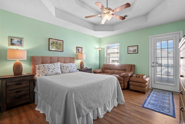 bedroom featuring multiple windows, hardwood / wood-style floors, a tray ceiling, and access to outside