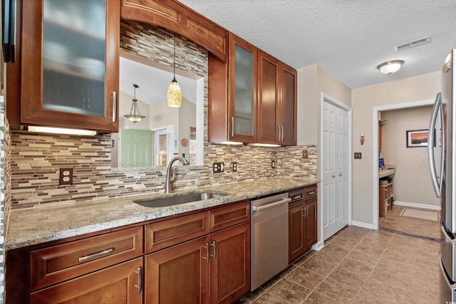 kitchen with light stone counters, appliances with stainless steel finishes, decorative light fixtures, and sink