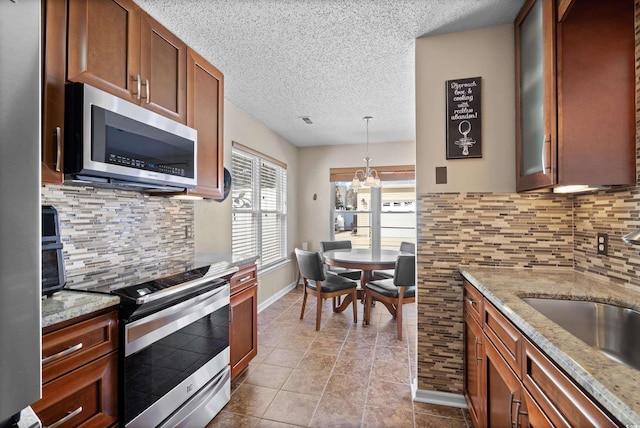 kitchen featuring sink, light stone counters, a textured ceiling, pendant lighting, and stainless steel appliances