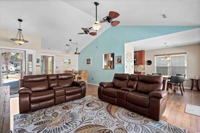 living room with ceiling fan with notable chandelier, high vaulted ceiling, a textured ceiling, and light wood-type flooring