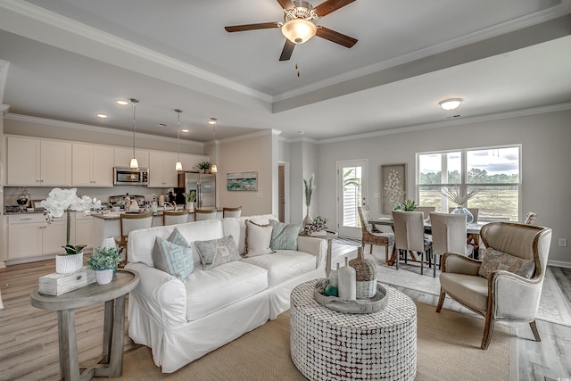 living area with light wood-style floors, ceiling fan, a tray ceiling, and crown molding