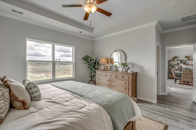 bedroom with a tray ceiling, ornamental molding, ceiling fan, and light wood-type flooring