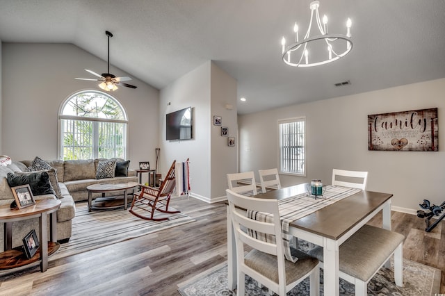 dining space with light wood-type flooring, ceiling fan with notable chandelier, vaulted ceiling, and a wealth of natural light