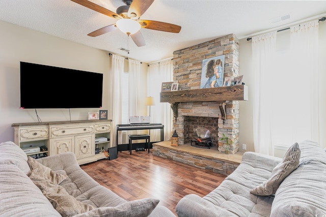 living room featuring ceiling fan, wood-type flooring, a fireplace, and a textured ceiling