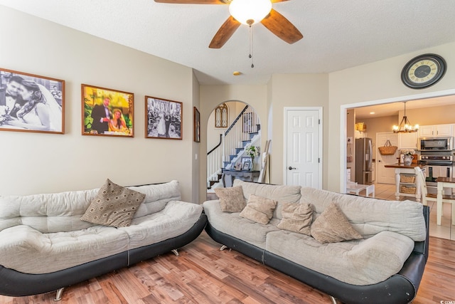 living room featuring ceiling fan with notable chandelier, a textured ceiling, and light hardwood / wood-style floors