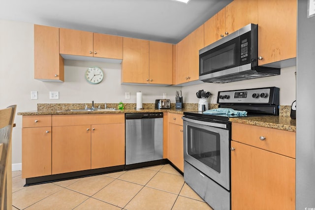 kitchen featuring sink, light tile patterned flooring, dark stone counters, and appliances with stainless steel finishes