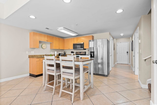 kitchen featuring stainless steel appliances, light tile patterned flooring, light brown cabinets, and an island with sink