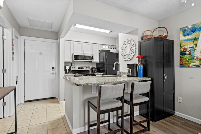 kitchen featuring sink, white cabinetry, light tile patterned floors, stainless steel appliances, and light stone countertops