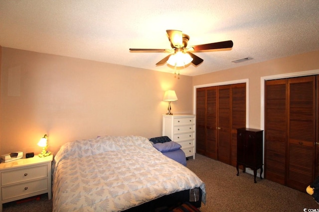 carpeted bedroom with ceiling fan, two closets, and a textured ceiling