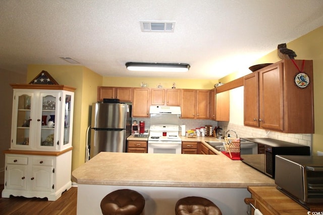 kitchen featuring sink, stainless steel appliances, tasteful backsplash, dark hardwood / wood-style flooring, and kitchen peninsula