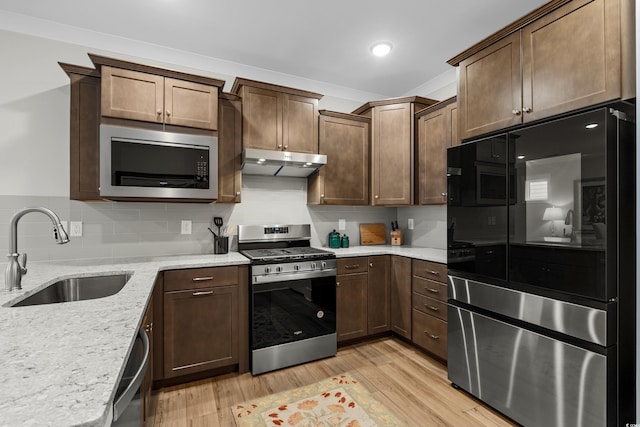 kitchen with sink, light stone counters, appliances with stainless steel finishes, light hardwood / wood-style floors, and backsplash