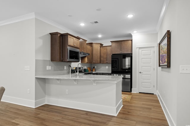 kitchen featuring light hardwood / wood-style flooring, backsplash, stainless steel microwave, a kitchen bar, and kitchen peninsula