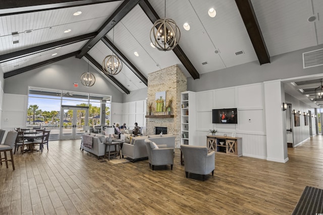 lobby featuring a stone fireplace, high vaulted ceiling, wood-type flooring, a notable chandelier, and french doors