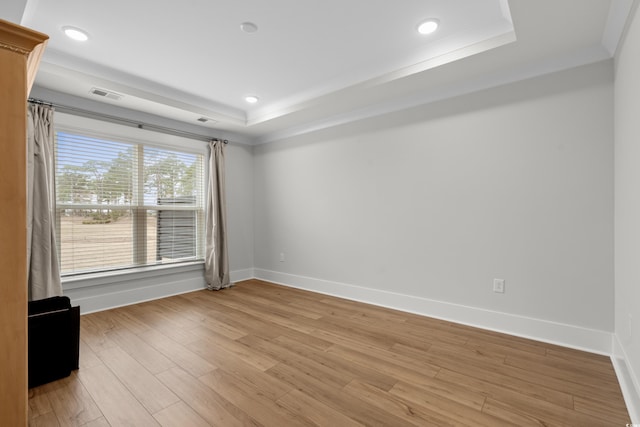 unfurnished room featuring crown molding, a raised ceiling, and light wood-type flooring