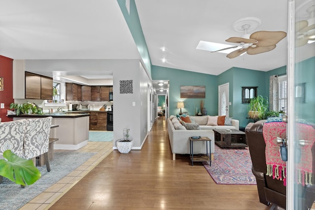 living area featuring ceiling fan, vaulted ceiling with skylight, light wood-type flooring, and baseboards