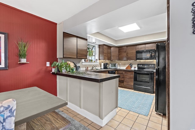 kitchen with a peninsula, black appliances, dark countertops, and light tile patterned flooring