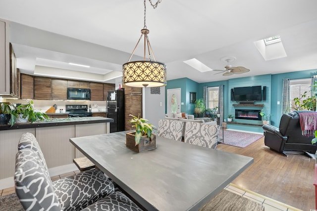 dining room featuring a skylight, a glass covered fireplace, light wood-style flooring, and a ceiling fan