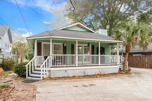 view of front of house with covered porch, roof with shingles, a chimney, and fence