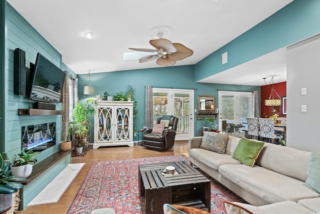 living area featuring lofted ceiling, ceiling fan, a fireplace, and wood finished floors