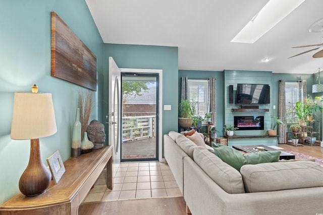 living area with a healthy amount of sunlight, a skylight, ceiling fan, and a fireplace