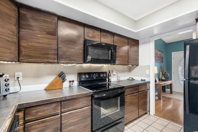 kitchen featuring light tile patterned floors, black appliances, dark brown cabinets, and dark countertops