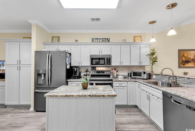 kitchen with sink, appliances with stainless steel finishes, a skylight, white cabinets, and decorative light fixtures