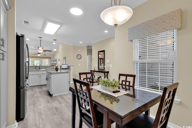 dining space with sink, ornamental molding, ceiling fan, and light wood-type flooring