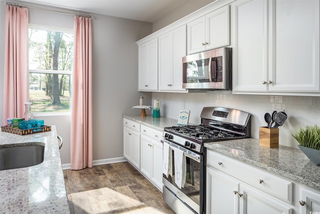 kitchen with stainless steel appliances, light stone countertops, white cabinets, and backsplash