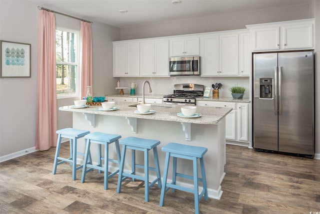kitchen with stainless steel appliances, a sink, white cabinetry, a center island with sink, and dark wood-style flooring