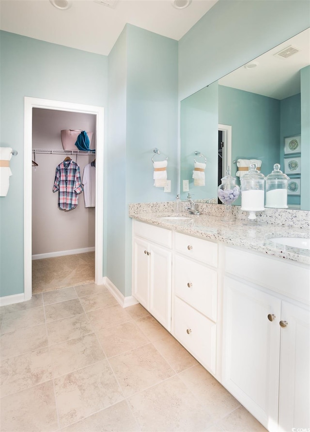 full bathroom with a spacious closet, double vanity, and baseboards