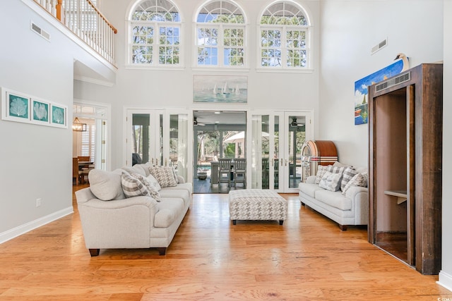 living room with a high ceiling, ceiling fan, light wood-type flooring, and french doors