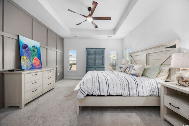 bedroom with light carpet, a raised ceiling, and ceiling fan