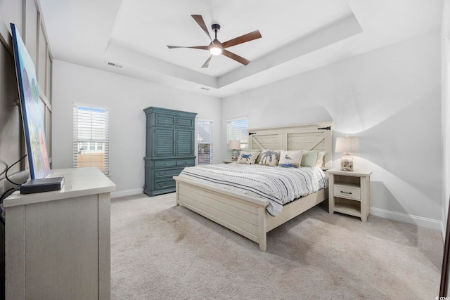 bedroom featuring light carpet, a tray ceiling, and ceiling fan