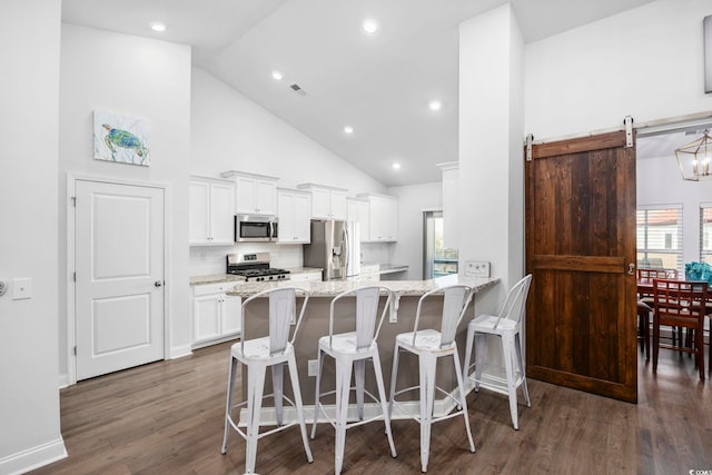 kitchen featuring a breakfast bar area, white cabinetry, stainless steel appliances, a barn door, and light stone countertops