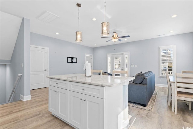 kitchen featuring a kitchen island, decorative light fixtures, white cabinets, light stone counters, and a healthy amount of sunlight