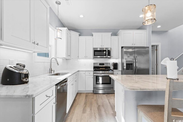 kitchen featuring appliances with stainless steel finishes, decorative light fixtures, white cabinetry, sink, and light stone countertops