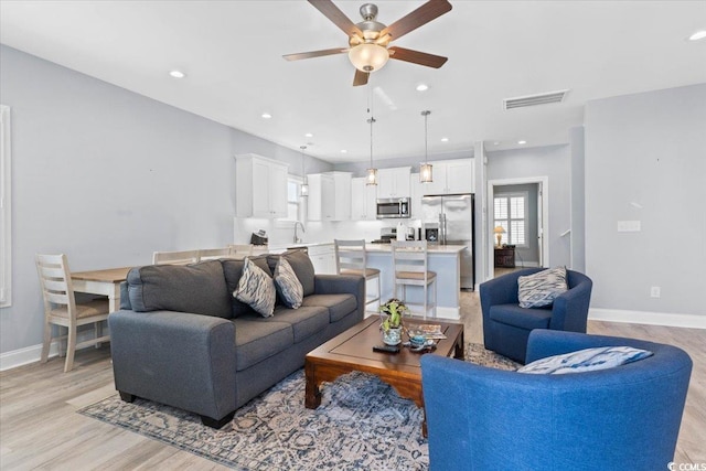 living room featuring sink, ceiling fan, and light wood-type flooring