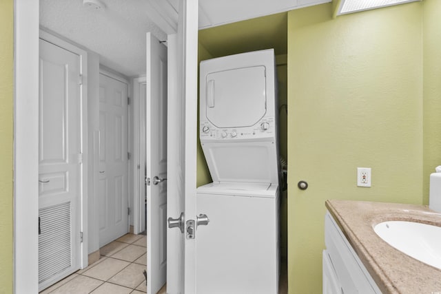 laundry room featuring sink, light tile patterned flooring, and stacked washing maching and dryer