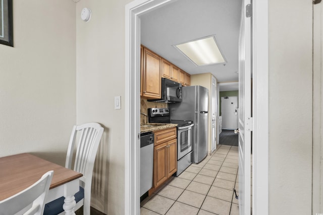 kitchen featuring light stone countertops, appliances with stainless steel finishes, light tile patterned floors, and backsplash