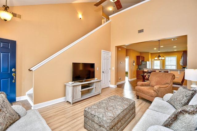 living room featuring high vaulted ceiling, ceiling fan with notable chandelier, and light wood-type flooring