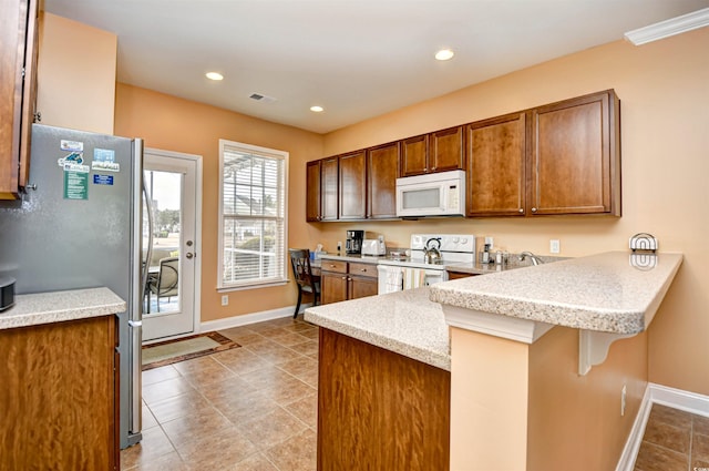 kitchen with white appliances, a kitchen bar, kitchen peninsula, and light tile patterned floors